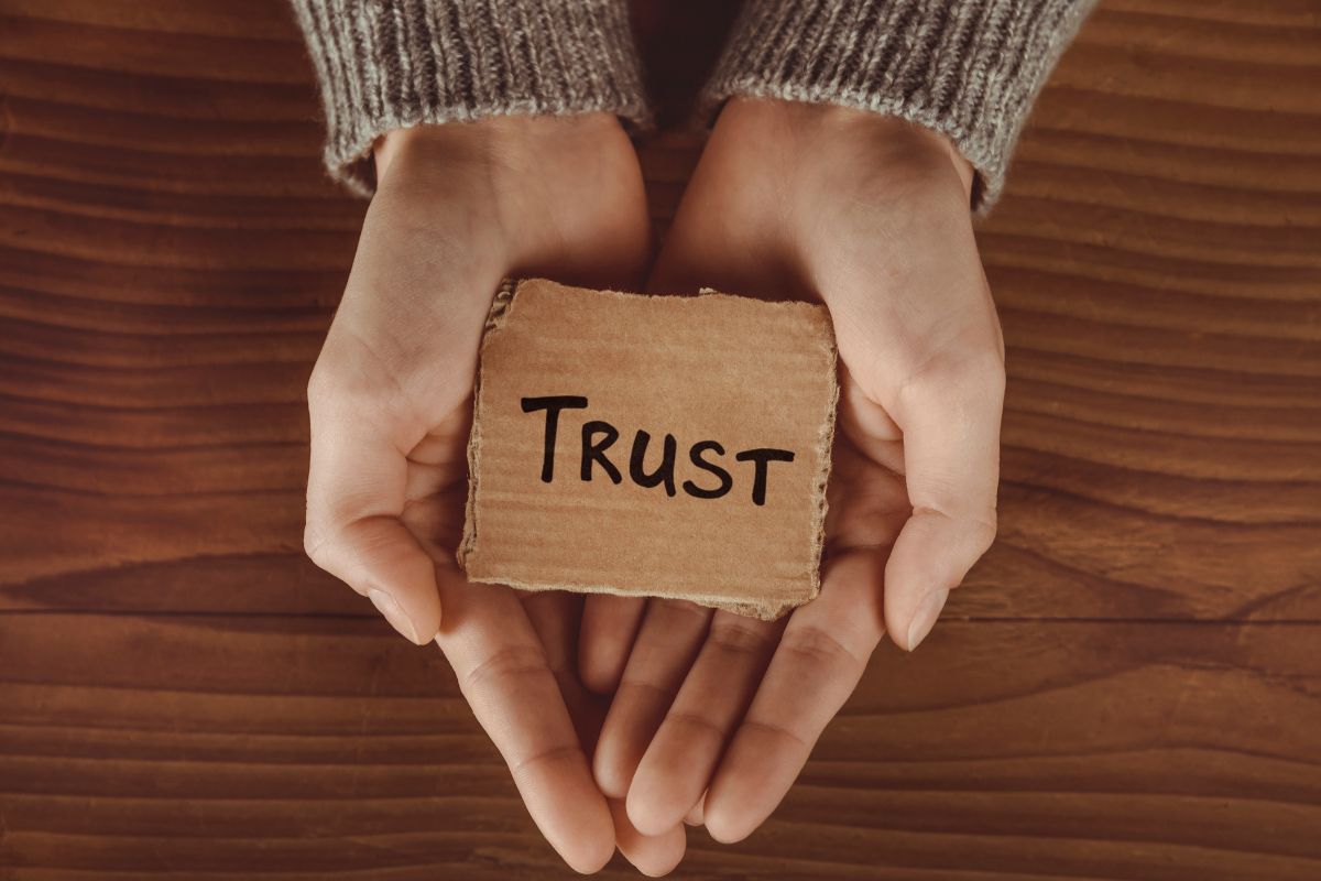 The image shows a girl's hand holding a piece of paper with a note which means trust the universe to provide financial opportunities helps bring it closer to reality.