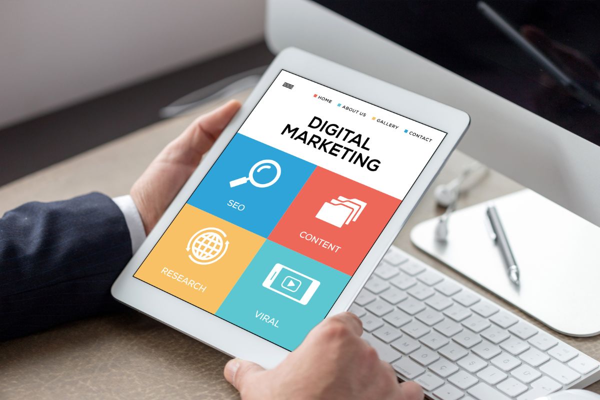 The picture tells about a computer set, a pen, and a man's hand using a tablet device with a screen display which refers to digital marketing managers helping businesses advertise online and could be a strong career path.