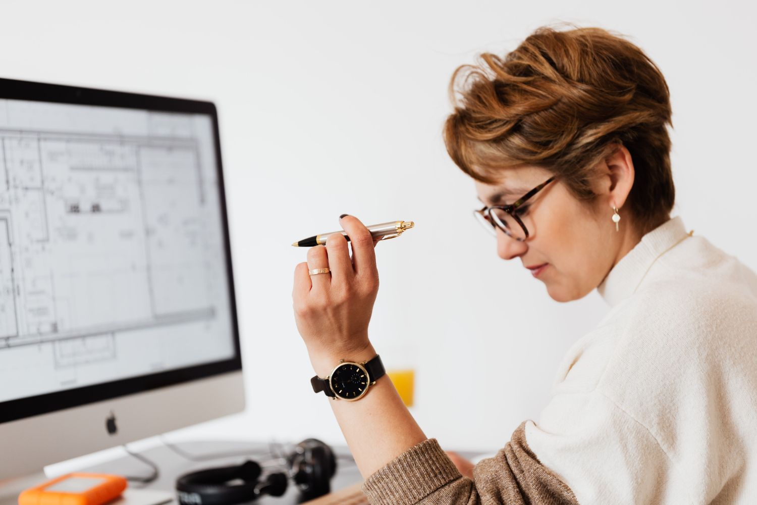 The photo shows a monitor screen with layouts and a girl holding a pen and analyzing it referring to solutions architects that figure out the best tools and systems to solve problems and a great remote job because most work is done online.