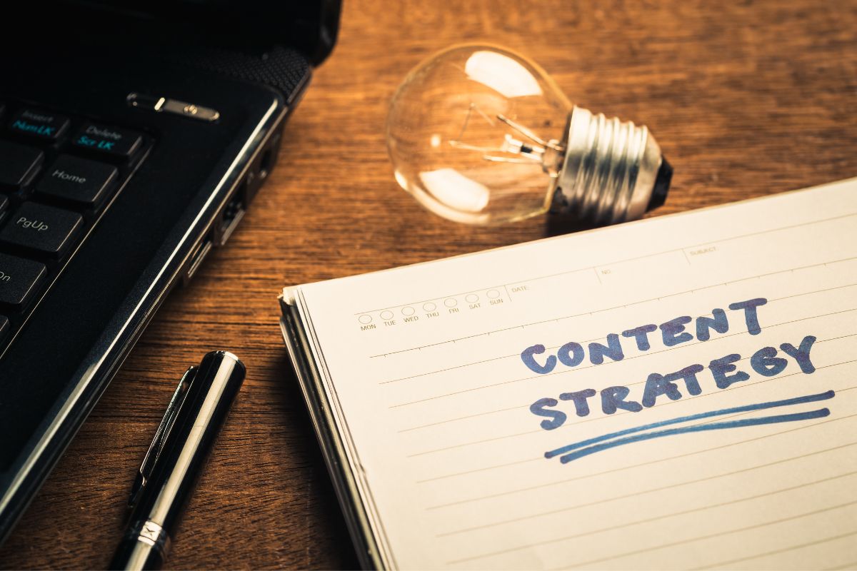 The picture tells about a bulb, a laptop, a pen, and a notebook with notes indicating to content strategies plan and manage online content for businesses and could be a good way to work from home.