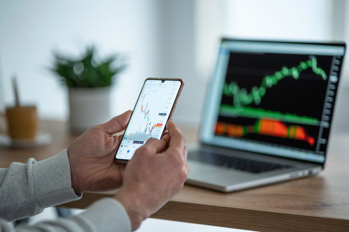 Image of a man doing stock trading on his phone and laptop.