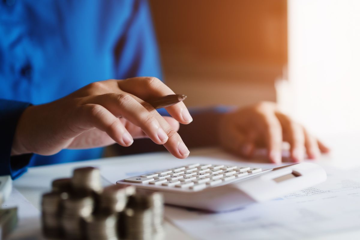 The image tells about coin stocks and a girl's hand calculating the papers referring to no spend month can improve budgeting skills that can make long-term savings easier.