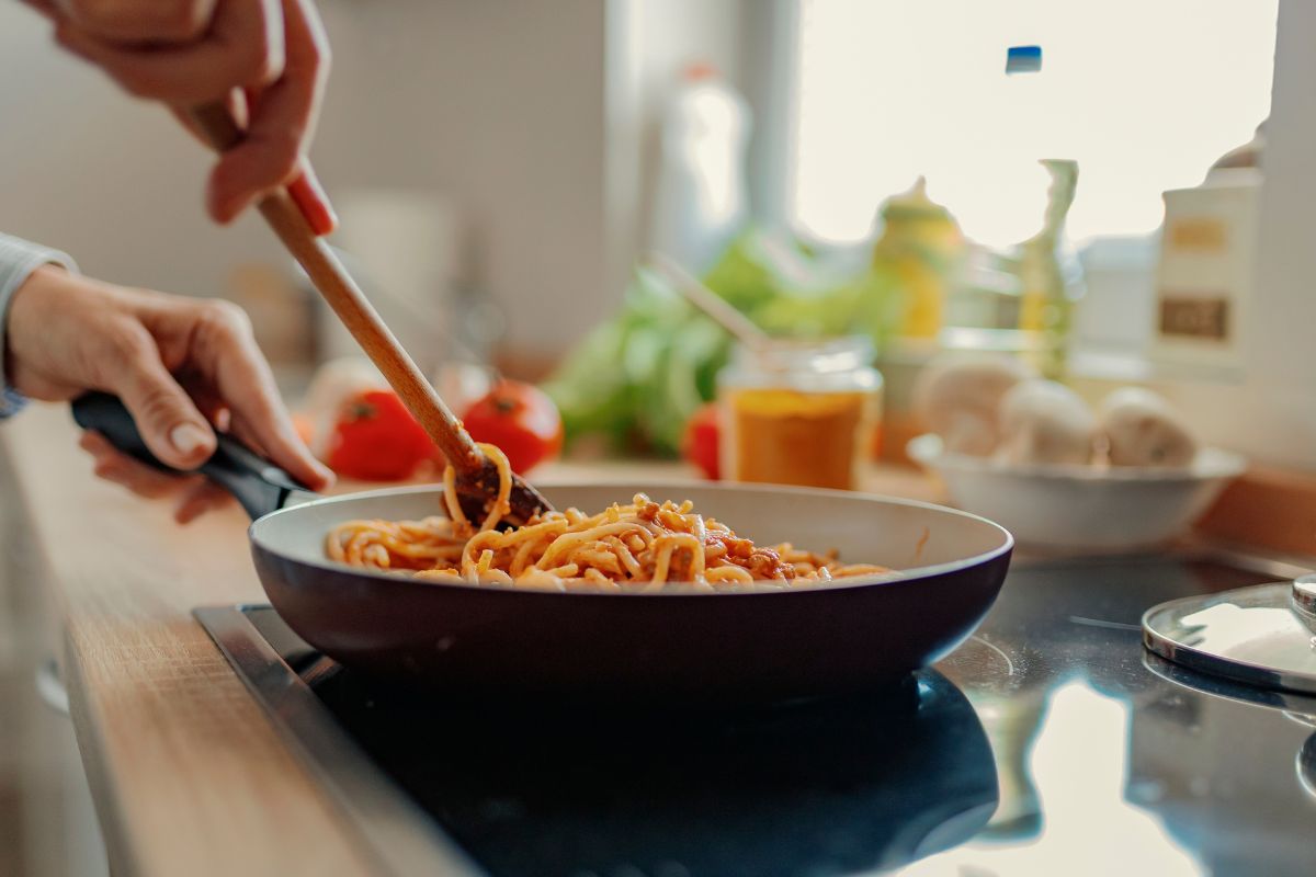 The picture shows ingredients at the kitchen and a girl's hand cooking a pasta which refers to no spend month encourages home-cooked meals that can lead to long-term savings and better health.