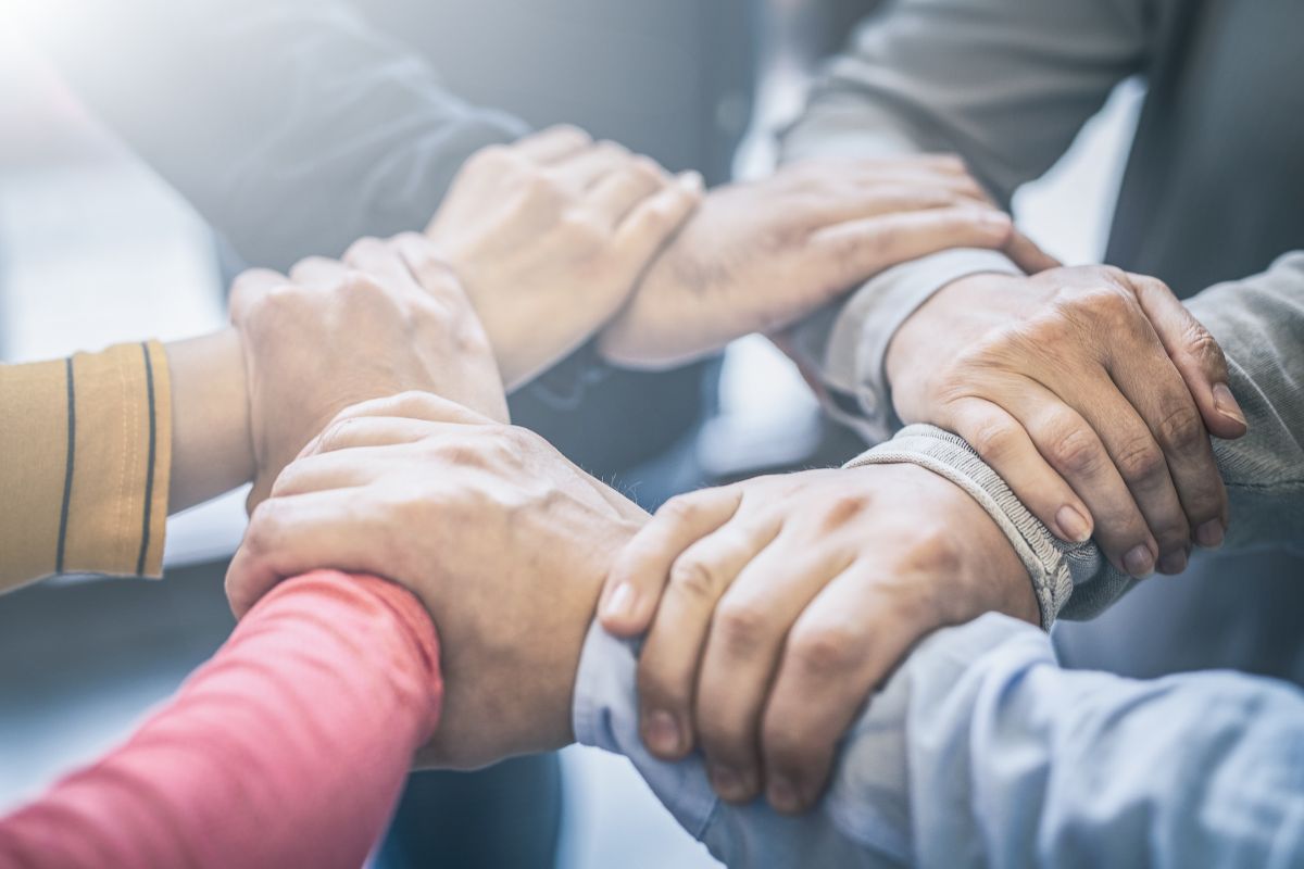 The picture shows a group of people joining hands together indicating that joining a savings community can inspire you to keep going and make the process more fun.