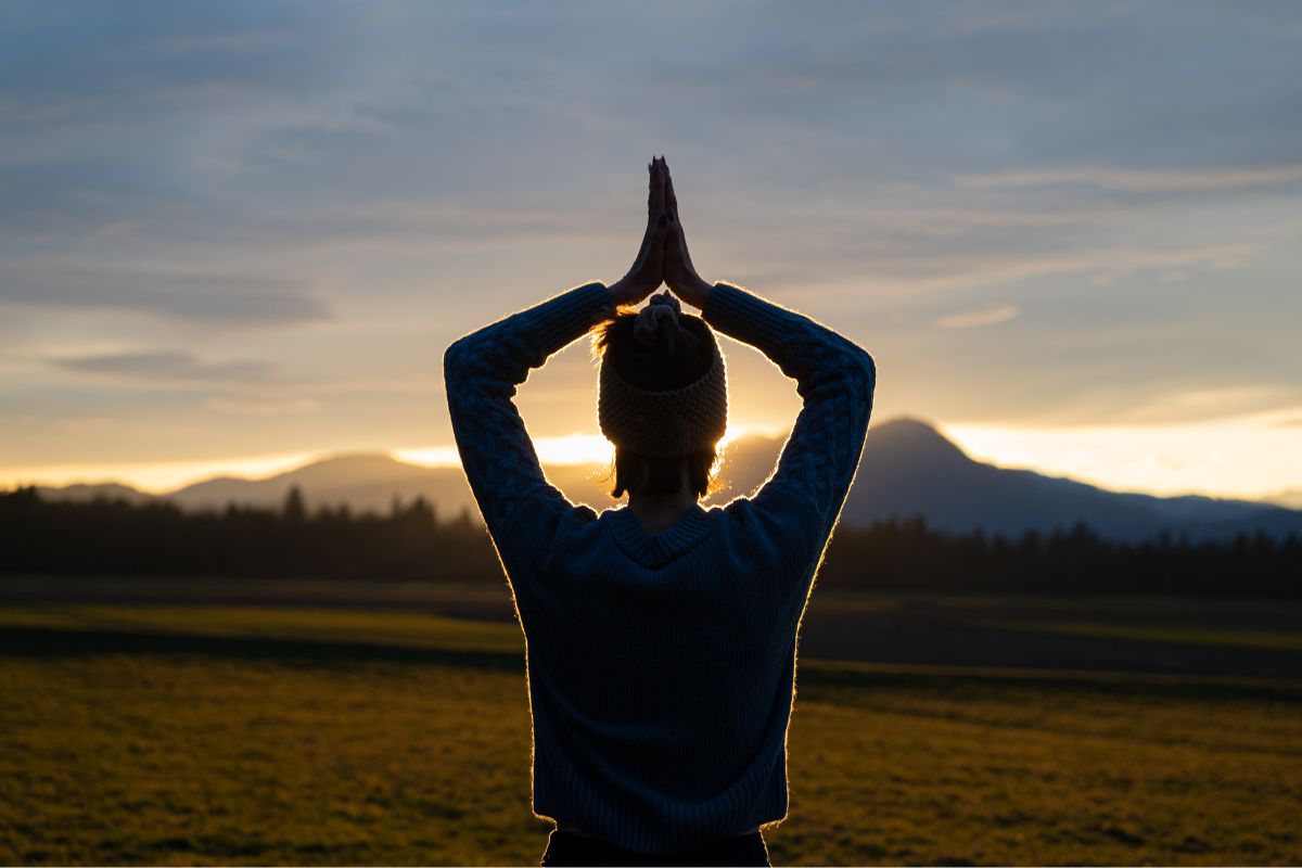 The photo shows a girl meditating in an open field referring to manifesting a prosperous mindset that helps you stay focused when savings get tough.