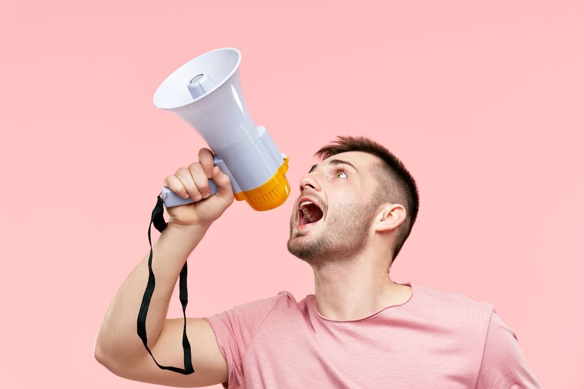 The image shows a man using a megaphone to speak your goals into existence making it easier to stick with your plan.