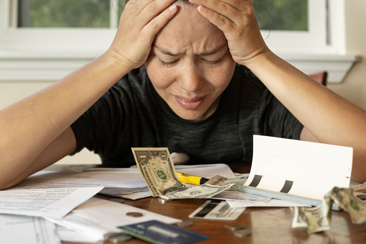 The picture tells about papers on the table, credit cards, coins, dollar bills, and a frustrated girl indicating it reduces financial stress and a more positive outlook on life.