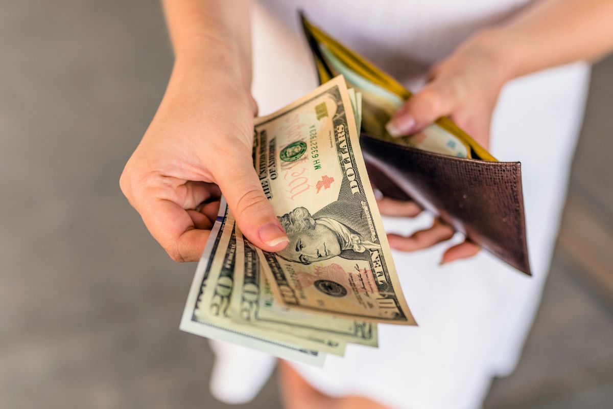 The photo shows a girl's hand holding a wallet and showing her money indicating that paying off debt creates discipline in financial habits and helps you make better money choices.