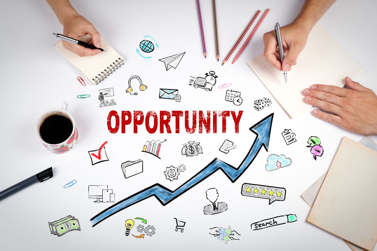 The photo shows a whiteboard with icons, pens, a coffee, papers, and two hands writing on the paper indicating that debt-free allows for more opportunities and gives you confidence in your financial future.