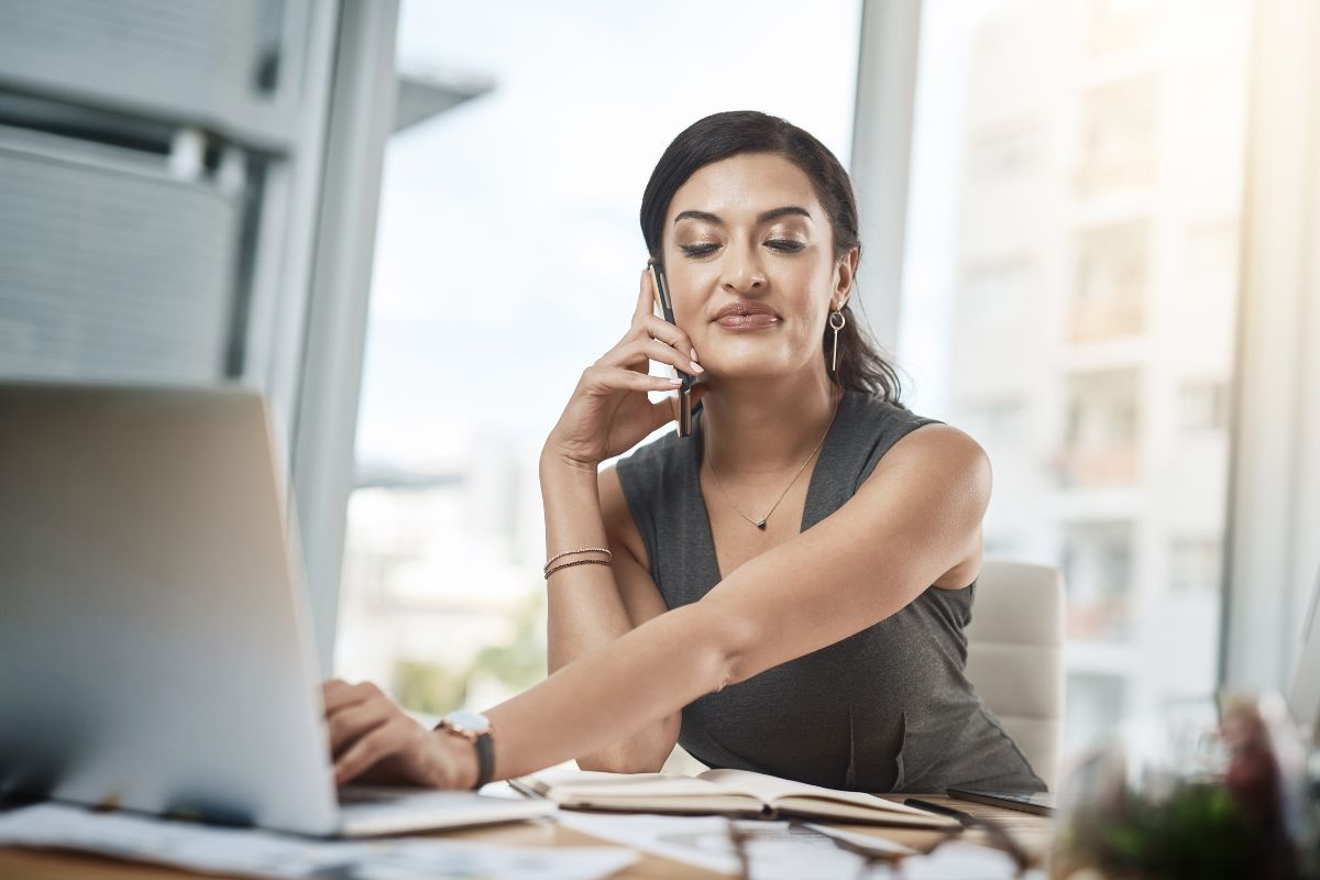 The image shows papers on the table, notebooks, and a girl using a laptop while having a call which refers to automating and outsourcing tasks to have more time to focus on making more money.