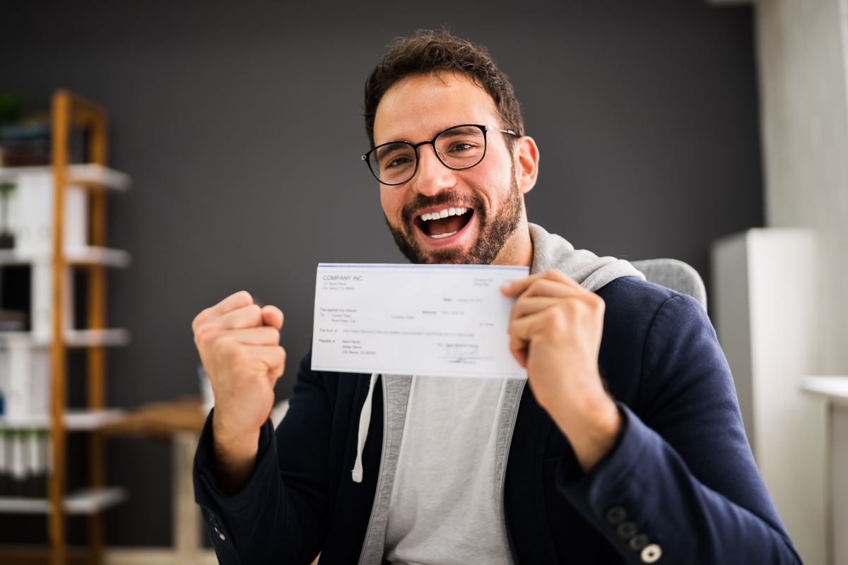 The photo shows a man holding a paycheck.