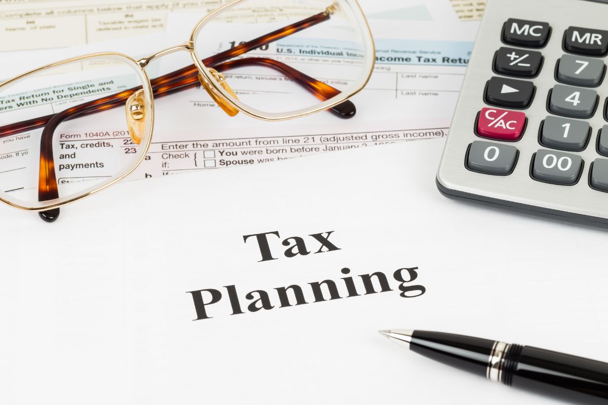 The picture shows papers with notes, a calculator, an eyeglass, and a pen which refers to planning for taxes and business expenses to keep your business strong and stress-free.