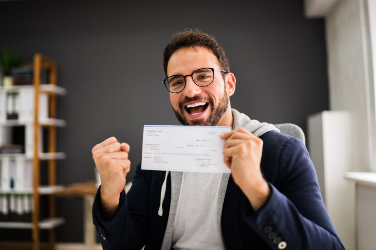 The picture shows a man happy while holding a payroll check which refers to the transition gradually before going to full-time giving you the best chance and success.