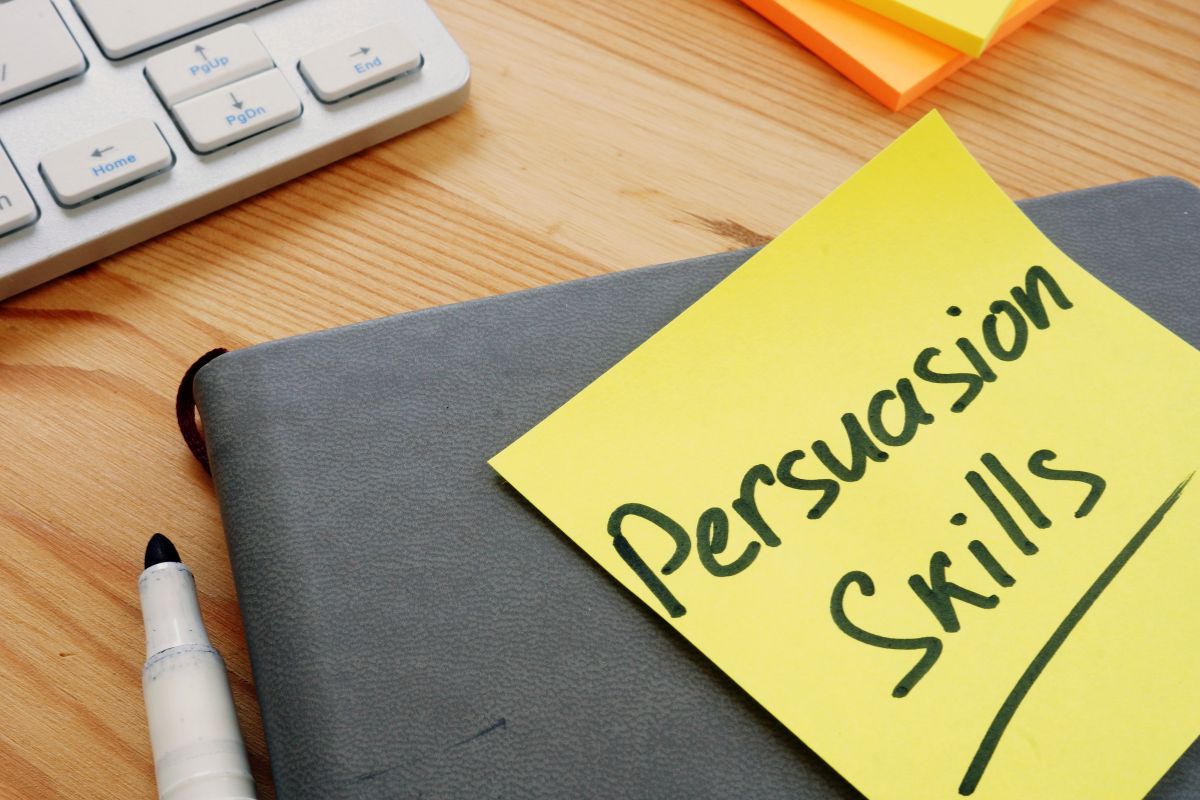The image shows a keyboard, sticker notes, a notebook, a marker, and a piece of paper with notes which refers to persuasion and negotiation that can turn opportunities into profit and secure long-term success.