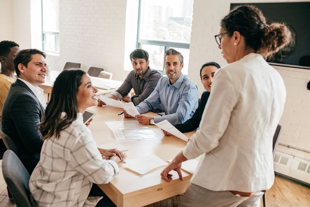 The picture tells about a group of members holding papers while listening to the girl in front which refers to leadership and team management helping businesses grow and earn high salaries.
