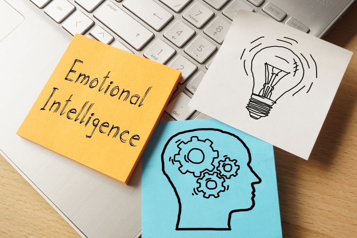 The photo tells about a laptop, and papers with icons and notes indicating that emotional intelligence leads to more opportunities and higher earnings. 