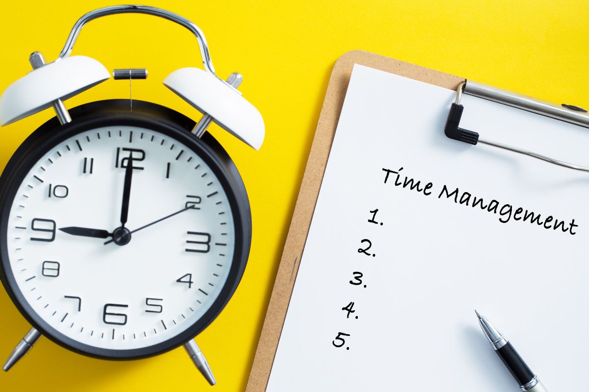 The photo of a clock, a pen, and a clipboard with notes referring to time management is key for entrepreneurs and high-earning professionals who juggle multiple projects.