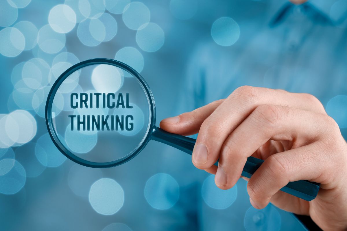 A man's hand magnifies the critical thinking wording.