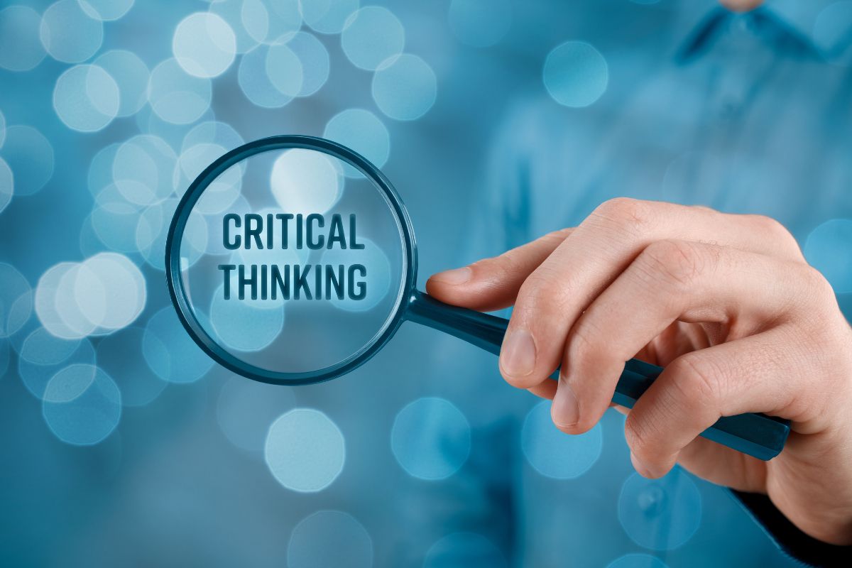 The photo shows a man's hand holding a magnifying glass with notes referring to critical thinking helps you analyze situations and make better decisions.