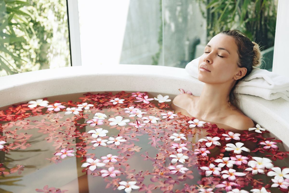 The picture tells about a girl taking a relaxing bath soaking with water and flowers at home referring to a home spa challenge is a great way to practice self-care without buying expensive products.