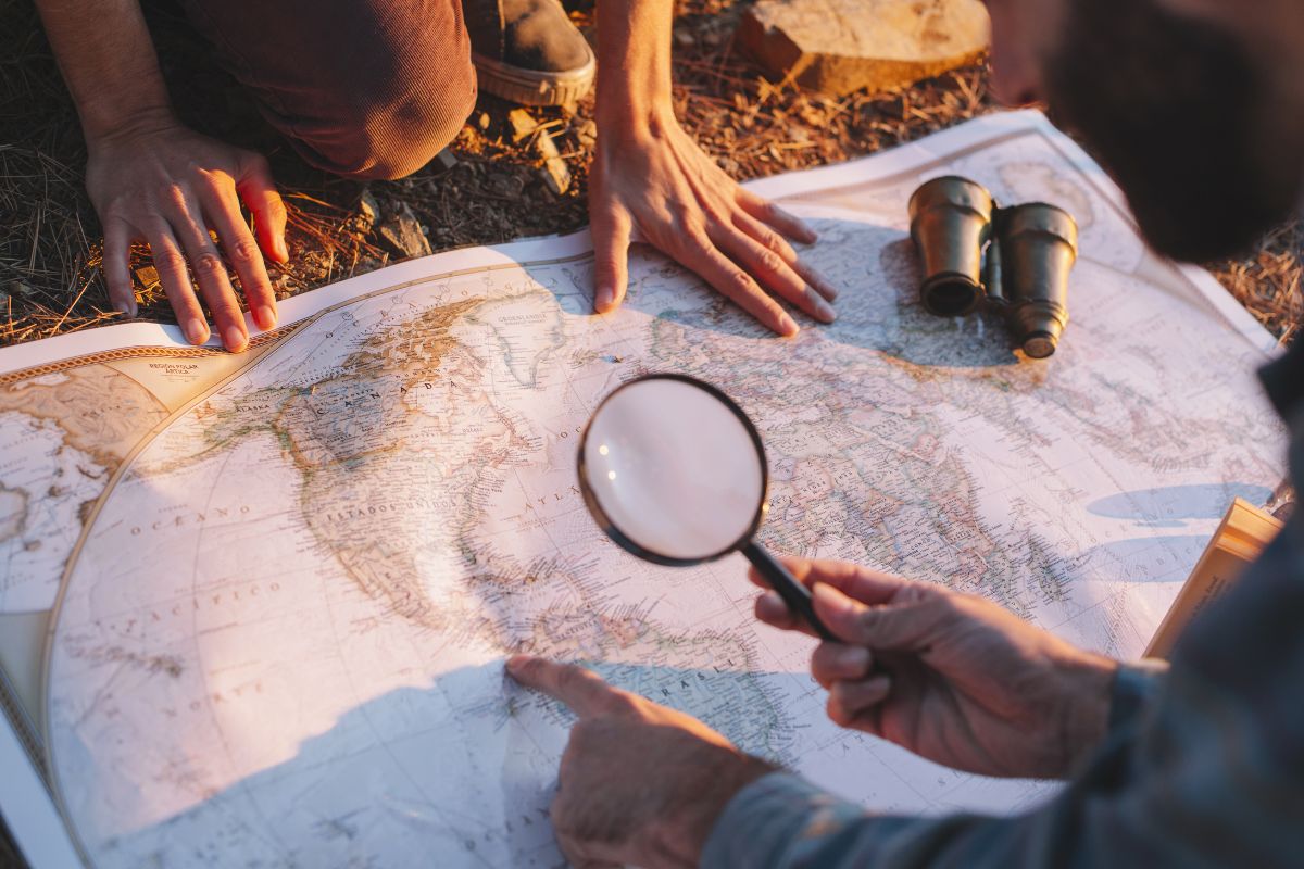 The picture is about a telescope and a man and girl holding a world map while using a magnifying glass which refers to creating a travel-at-home day as a fun way to break routine and try something new without spending money.
