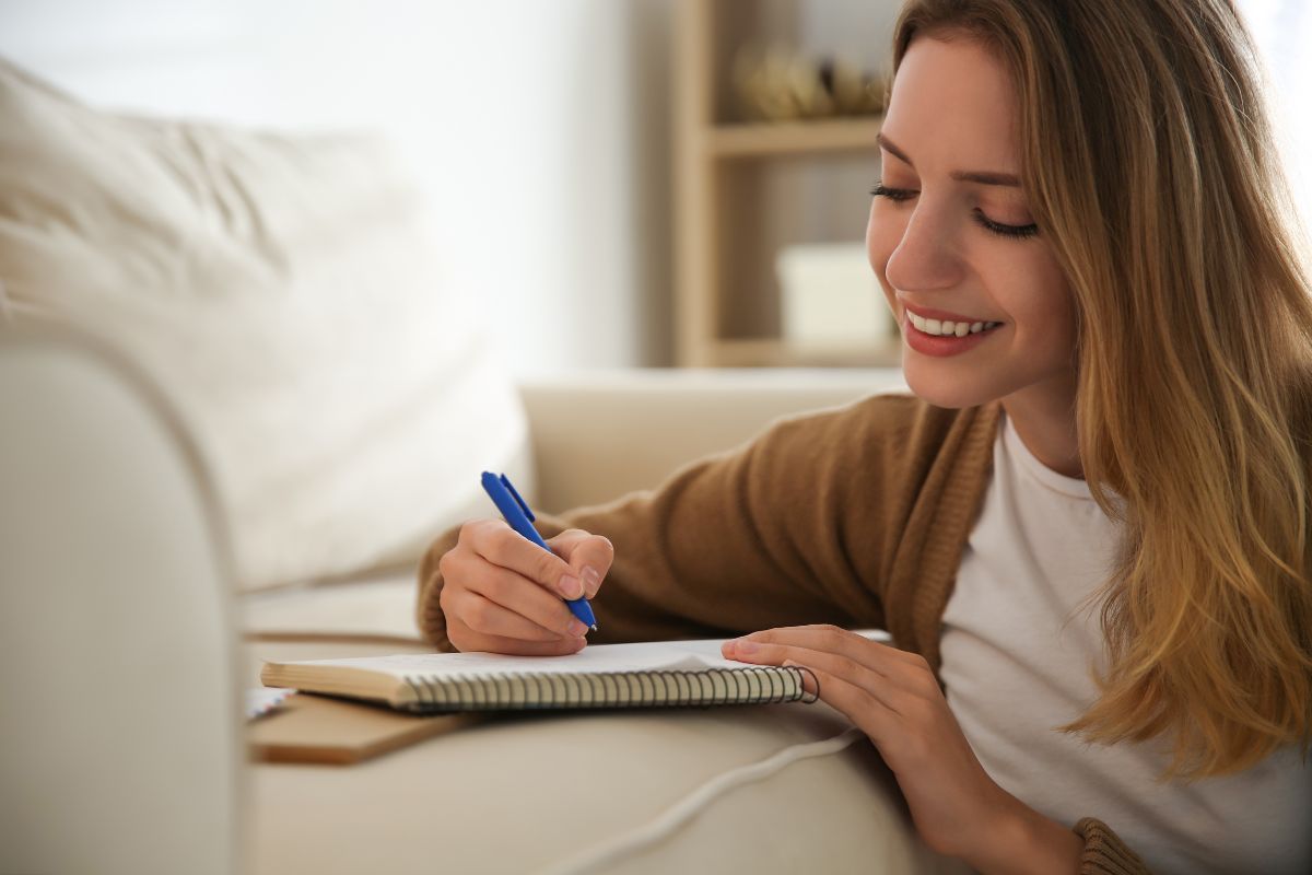 The image shows a girl writing in the notebook which refers to write  letters to your future self can be a powerful habit for self-improvement.