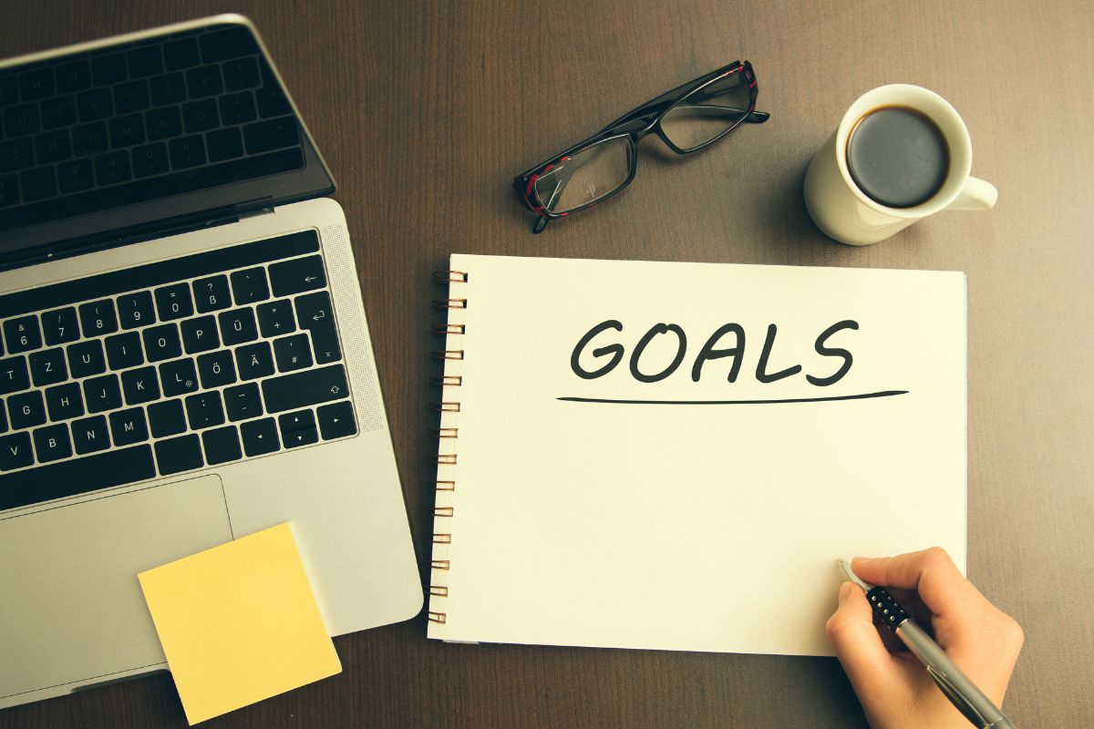 A woman's hand writing goals on a notebook.