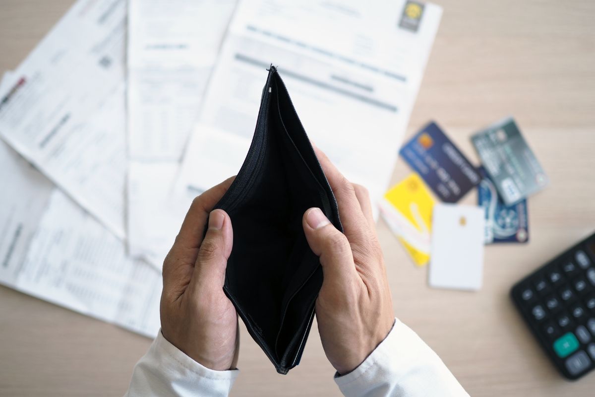 The picture tells about papers, cards, a calculator, and a man's hand opening an empty wallet indicating that avoiding debt is one of the best ways to reach financial freedom faster.