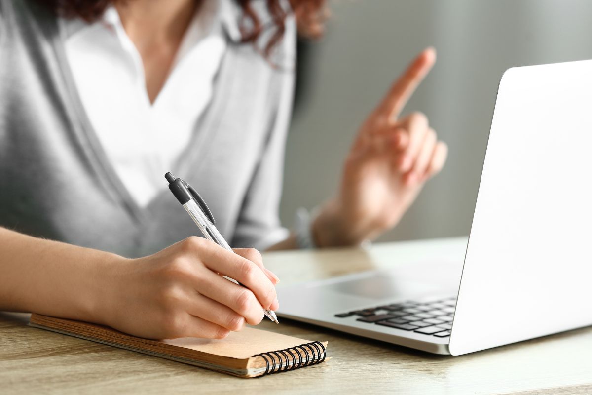 The picture shows a laptop and a girl taking notes which refers to note feeling before making a purchase can help you stop unnecessary spending.