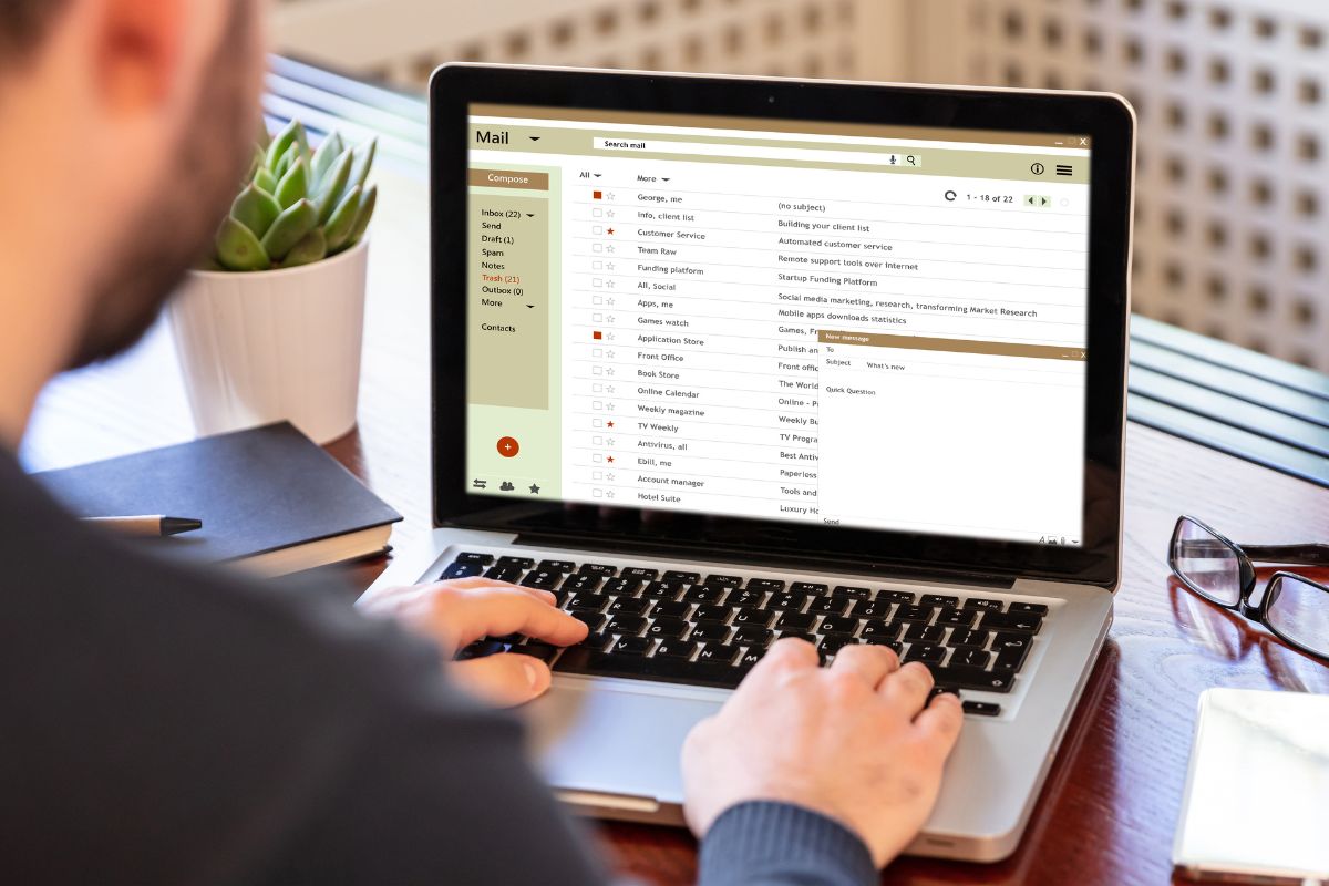 The image tells about a plant, an eyeglass, a notebook, a pen, and a man using a laptop referring to unsubscribing from marketing emails and alerts helps keep spending under control without constant pressure to shop.