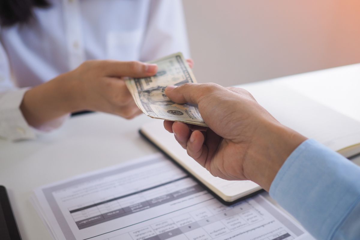 The photo tells about a paper with notes, a notebook, and a man's hand handing dollar bills to the girl which refers to the use of cash instead of credit creating a stronger connection to how much money is actually being spent.