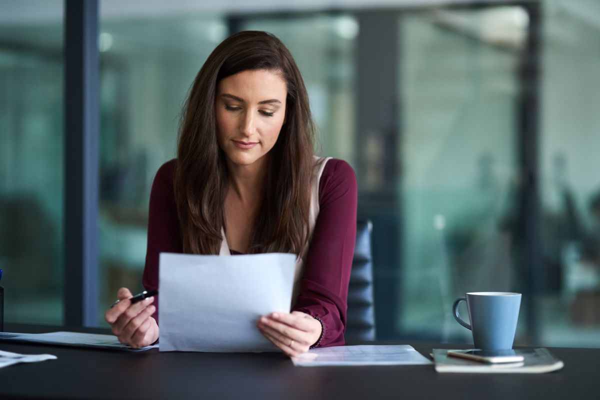The photo tells about a phone, a mug, papers on the table, and a girl checking on a paper to identify specific situations that encourage overspending gives you the power to change them.
