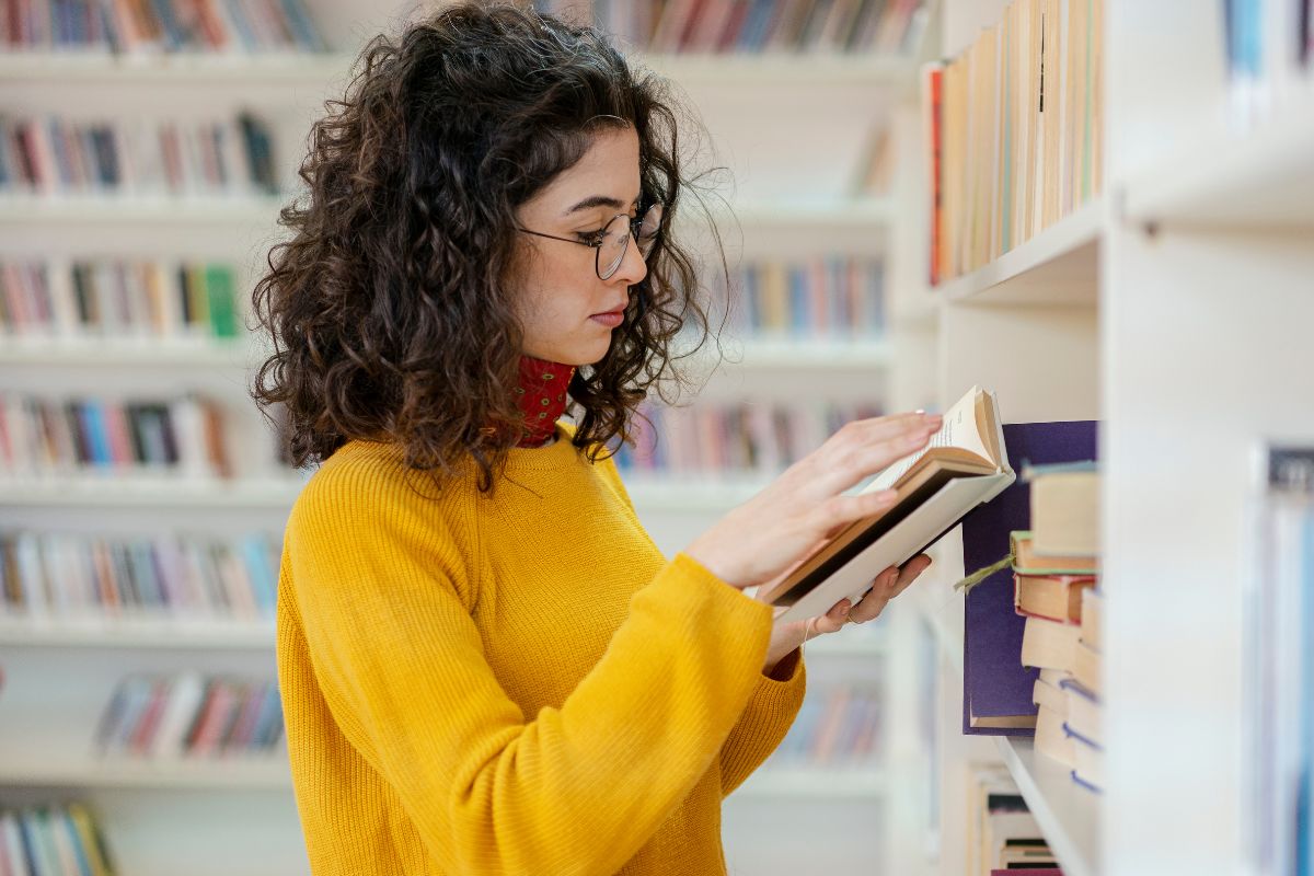 The image shows a woman reading a book at the library.