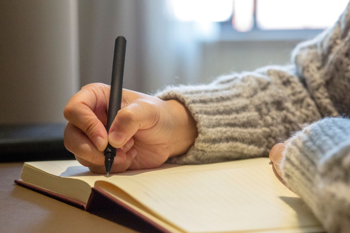 An image shows a woman's hand creating a list in a notebook.
