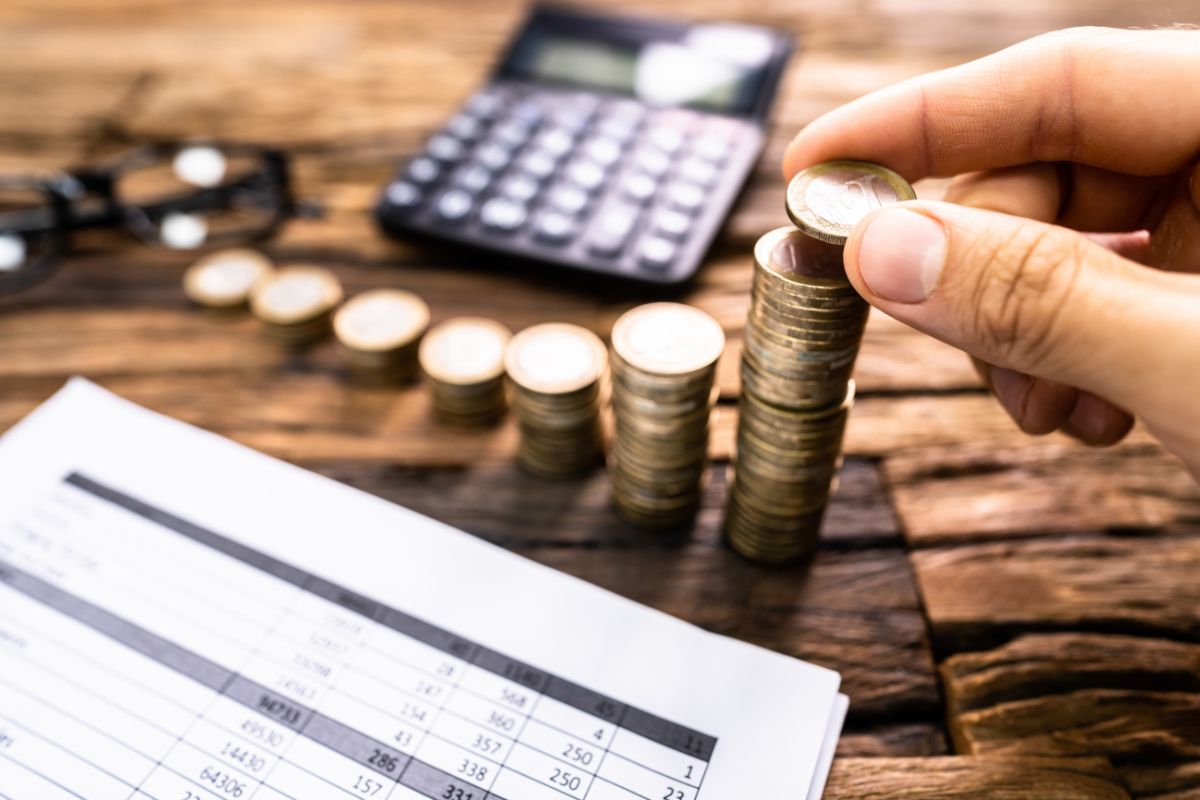 The picture shows a calculator, coins, eyeglasses, papers with notes, and a man's hand putting a coin referring to how creating multiple streams of income can set your family up for long-term financial success. 