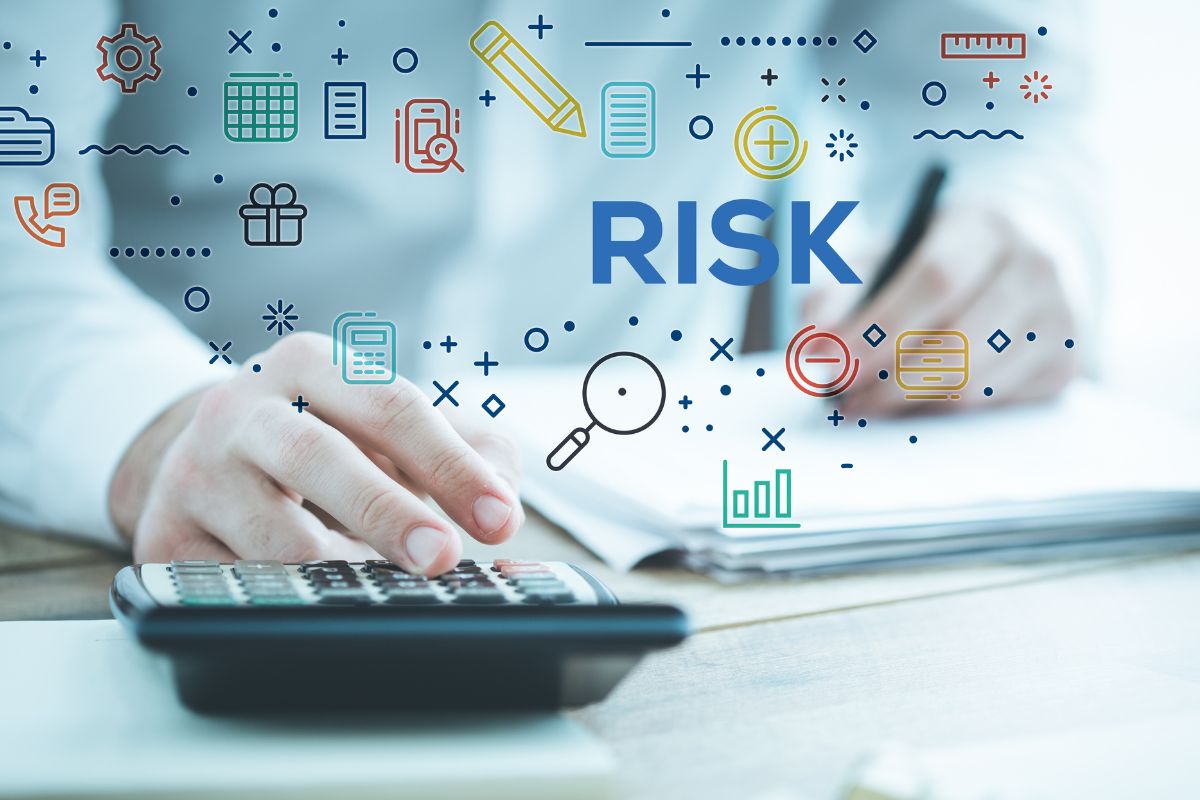 The photo shows visual icons and a note, papers on the table, and a man's hand calculating while writing on the paper indicating that taking calculated risks can lead to huge financial rewards.