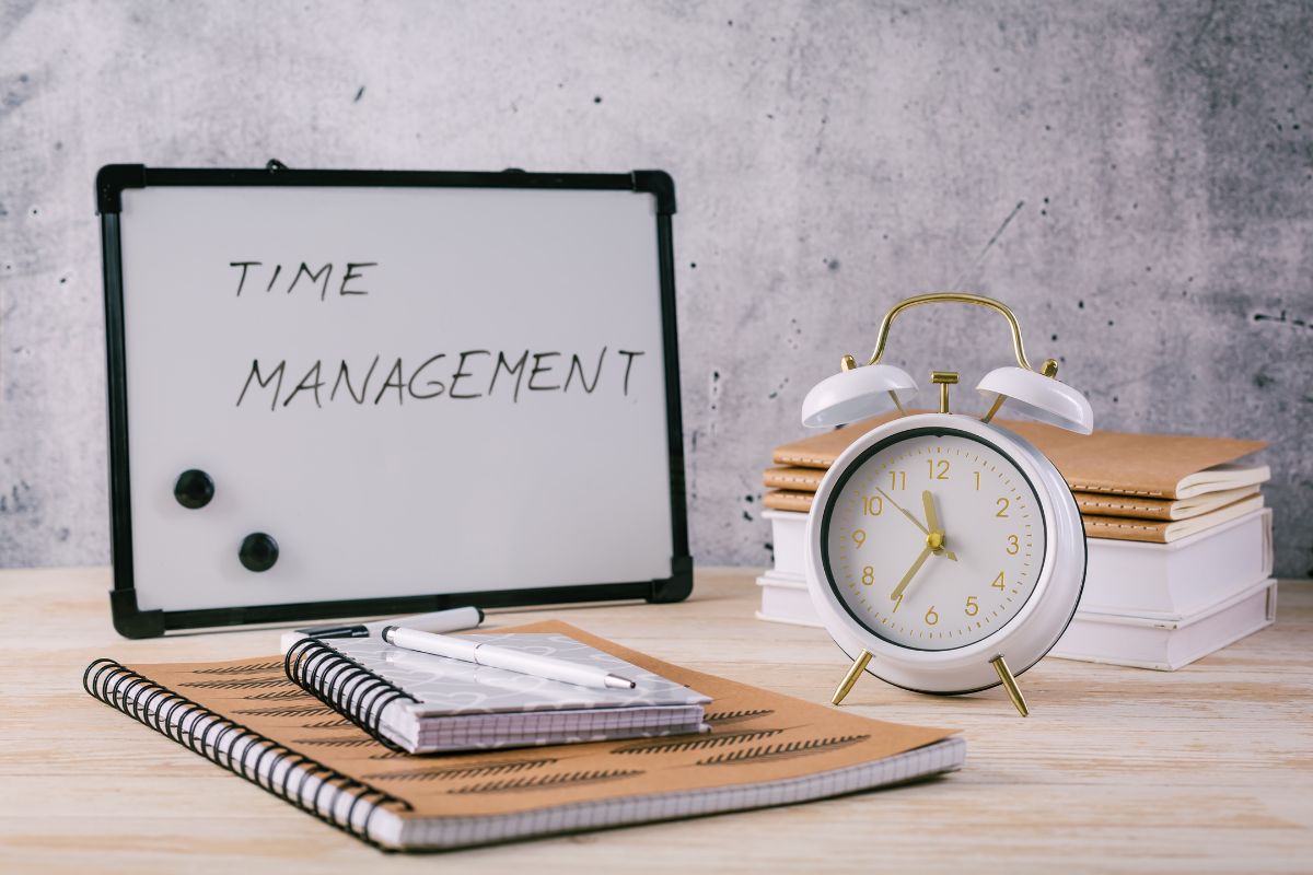 The image tells about notebooks, a clock, a pen, and a board with notes referring to developing strong time management skills that help you get more done and more closer to financial success.