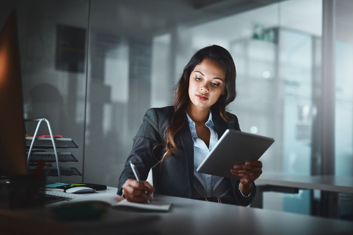 The image shows a girl holding a tablet device while writing in the notebook which means building and maintaining a strong work ethic helps grow wealth over time.