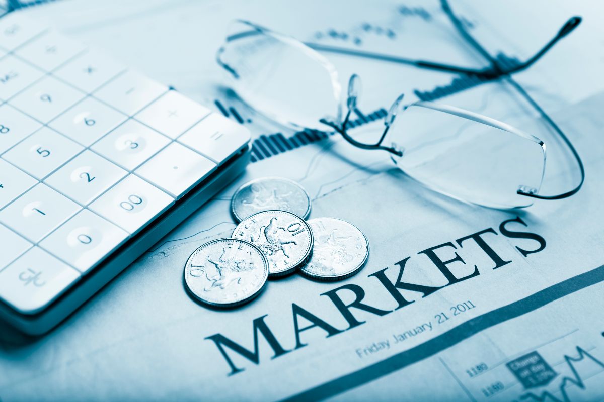The picture tells about papers with graphs and notes, an eyeglass, coins, and a calculator referring to how adapting to changing market conditions helps protect wealth and create new opportunities.