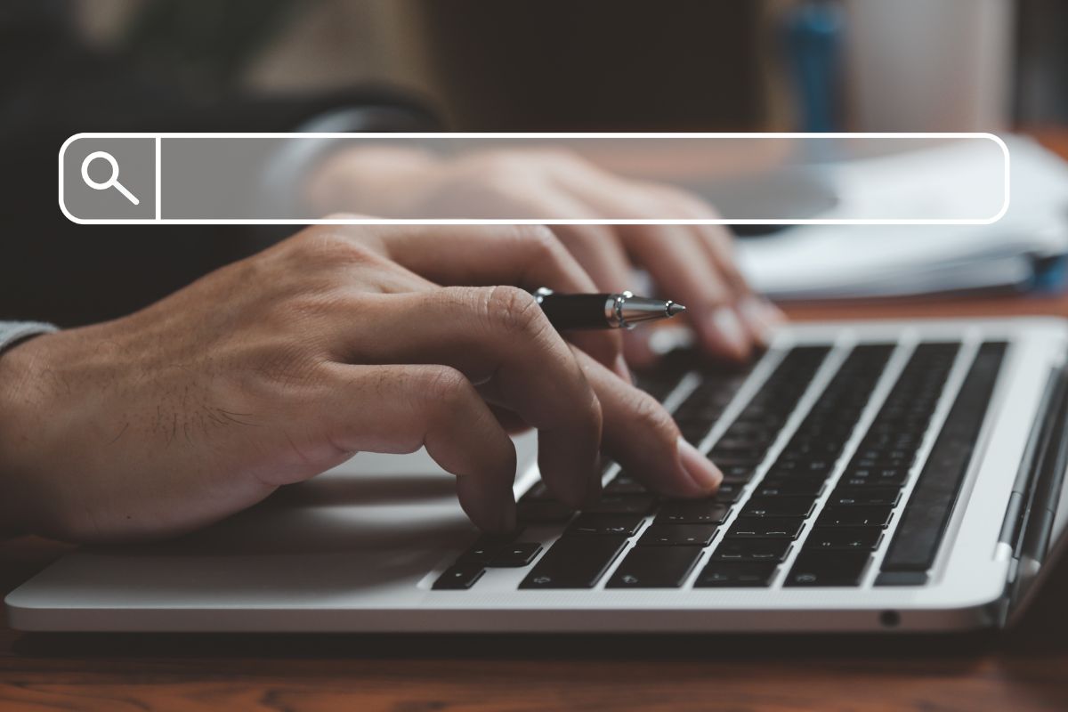 The image tells about a man's hand typing on the laptop with a search icon indicating to find all of the millionaire habits to reach financial success.