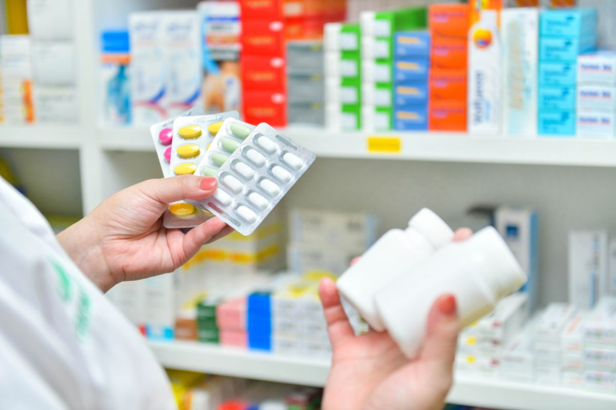 The image shows medicines displayed at the corner and a girl's hand holding two brands of medicines which refers to buying generic over-the-counter medications in bulk as a simple way to cut medical costs without sacrificing quality.
