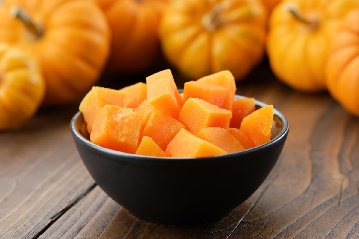 The image shows fresh pumpkins and a bowl of sliced pumpkins indicating that stocking up on seasonal items is an easy way to keep grocery costs down.
