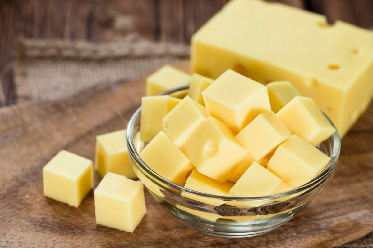 The photo tells about a bowl of cube cheese and a large cheese indicating that buying large blocks of cheese is a great trick for stretching your grocery budget.