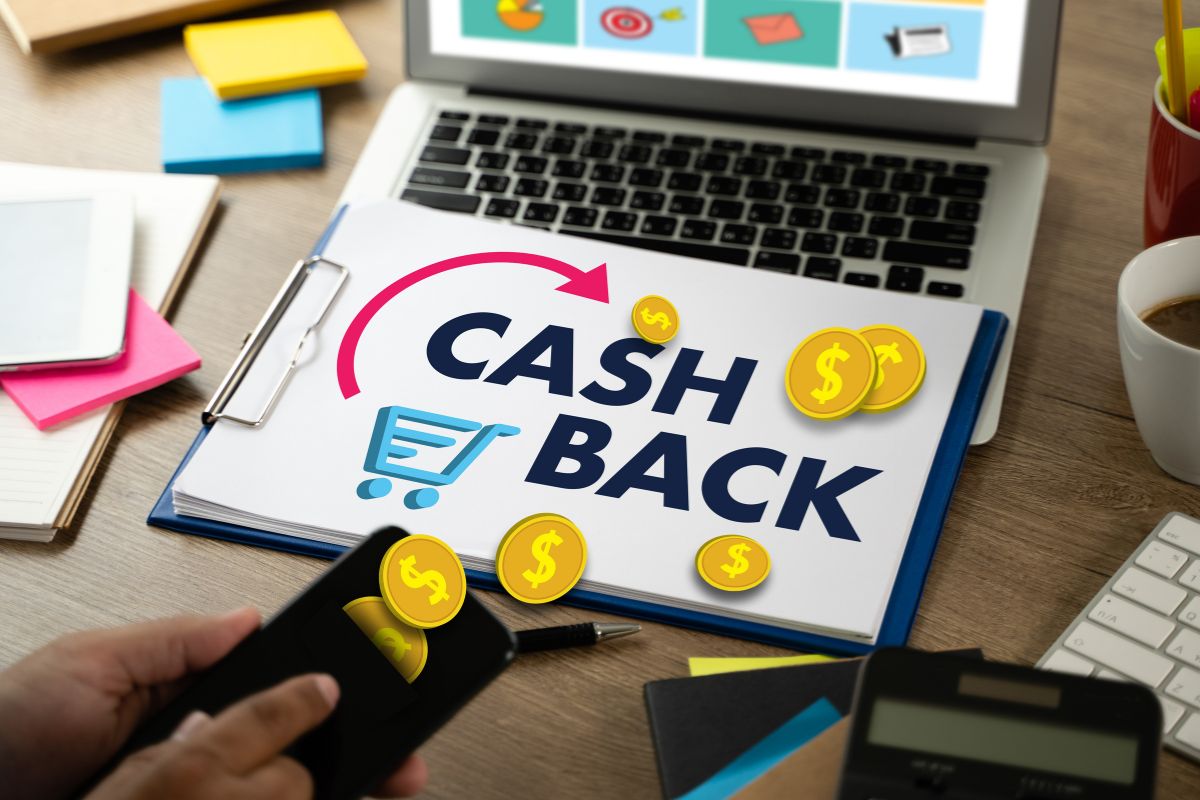 The picture tells about sticker notes, a laptop, a calculator, a clipboard with notes, and a man's hand holding a phone with a coins icon which refers to taking advantage of grocery cashback apps that help you get money back on everyday purchases that add up over time.
