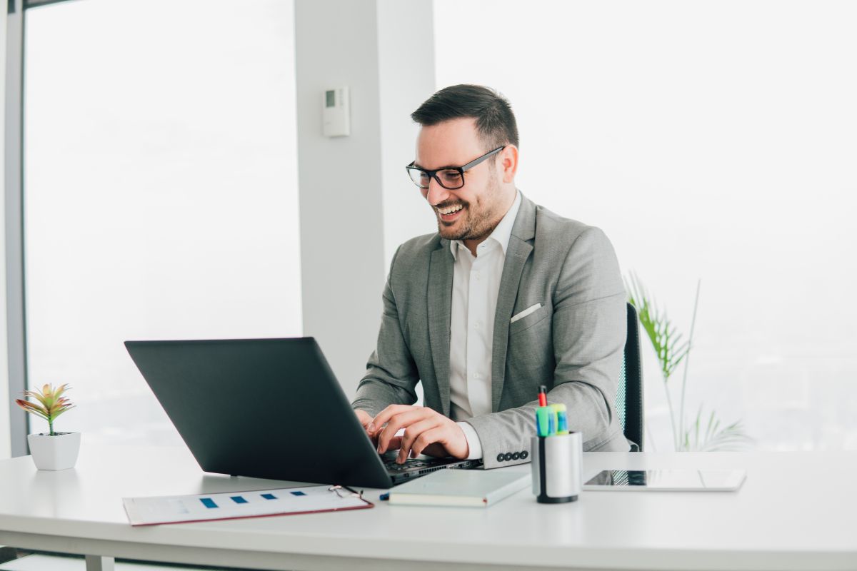The photo shows papers, a notebook, a tablet device, pens, and a man using a laptop referring to the use of the Pomodoro on Steroids technique helps maintain momentum and finish income-generating work faster.