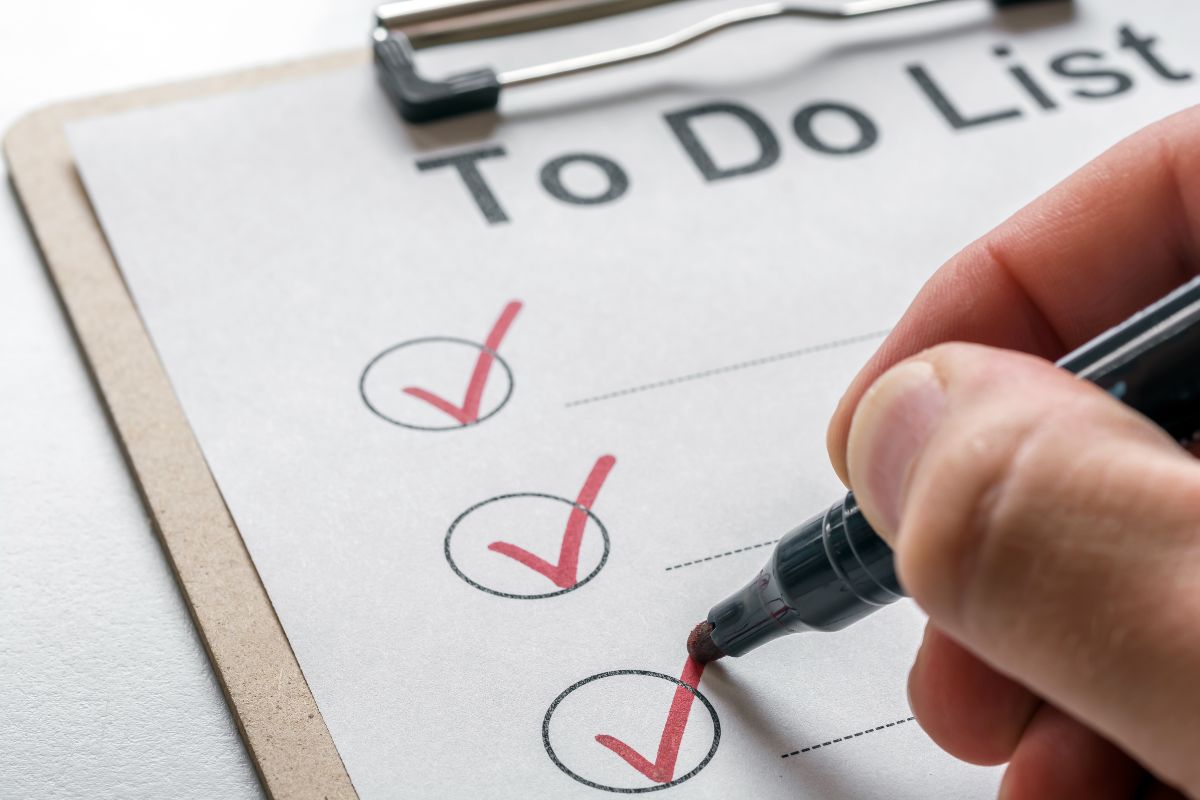 The photo shows a man's hand checking the clipboard with a paper referring to the use of a reverse to-do list to keep time management on point and help prioritize income-generating activities.