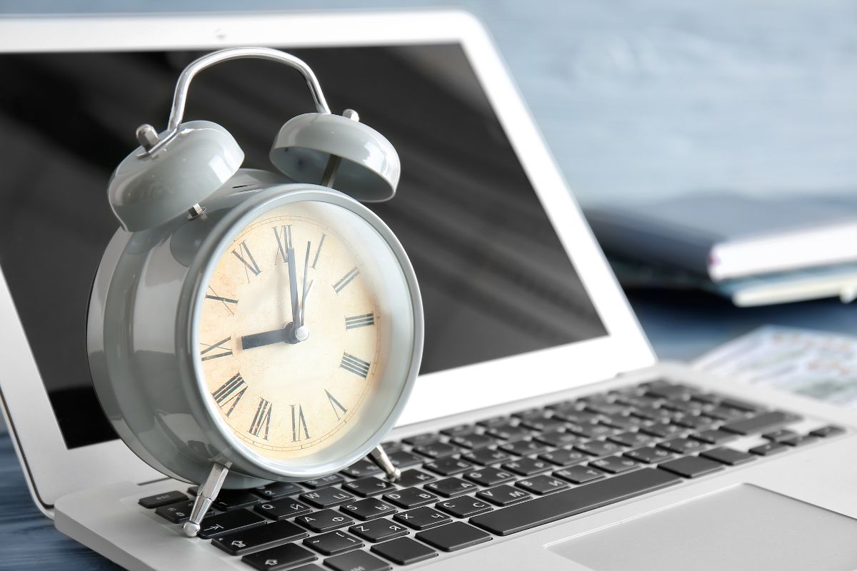The picture shows a notebook, a laptop, and a clock which means that creating high-value task alarms leads to better productivity and stronger earnings.