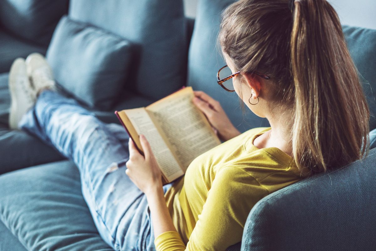 The picture of a girl relaxing on the couch while reading a book indicates to set a no-work buffer can improve focus, decision-making, and long-term earnings.