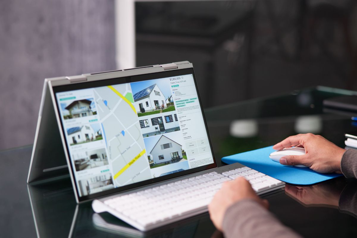 The photo tells about a man's hand using a laptop with a screen display indicating that selling digital land in virtual worlds is an online side hustle that could turn into a big opportunity.