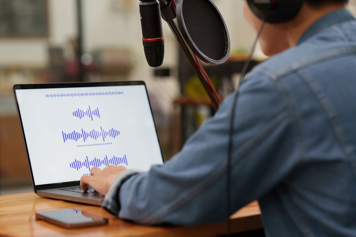 The photo shows a man recording his voice while editing on the laptop referring to curating and selling niche sound effects that can be a passive income source once your sounds are online.